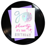 the words go shawty it's your birthday in shiny holographic rainbow foil with pink accents & a shiny disco ball for the o on top of a purple envelope. block printing by Niki Baker with foreignspell from hand-carved stamps & song lyrics.